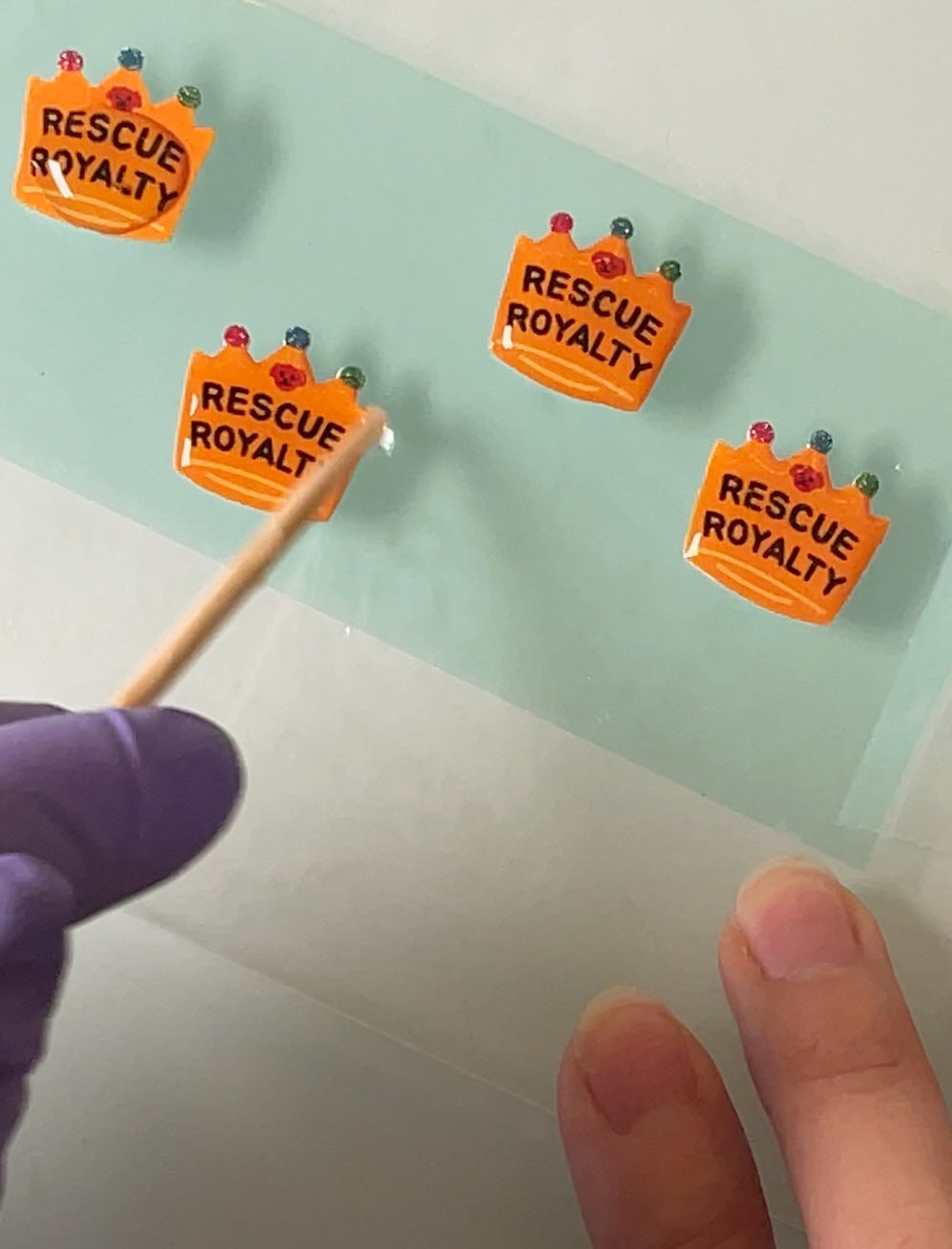 Four crown shaped dog charms for personalized dog collars or leashes with 'Rescue Royalty' text being covered with resin.