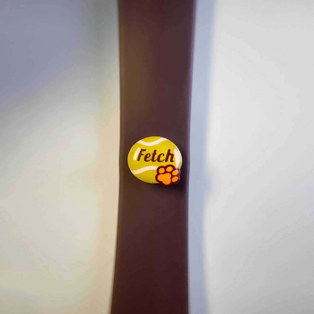 Charm with 'Fetch' text on a yellow tennis ball design with a yellow paw, attached to a brown dog leash.