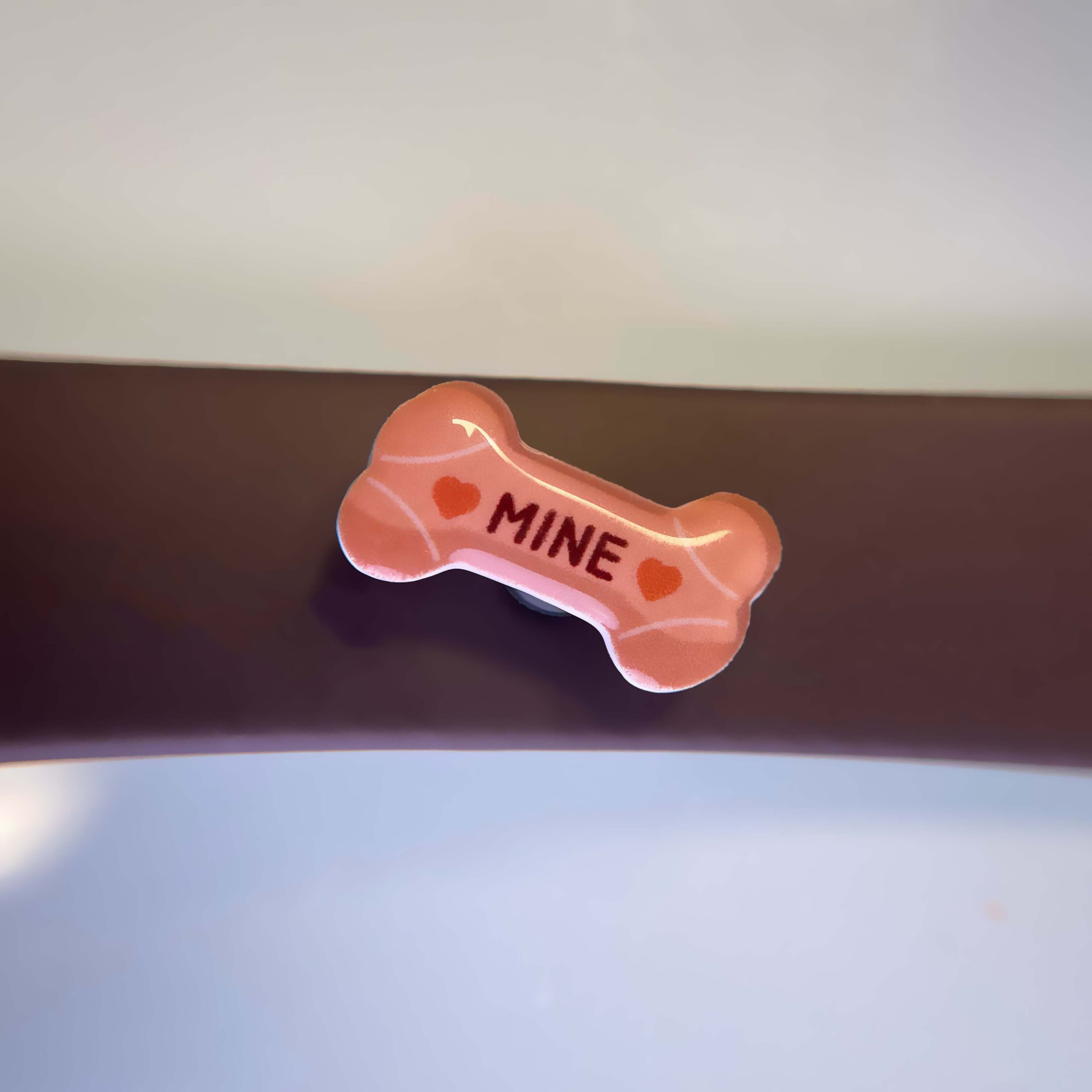 Beige milk bone charm with 'MINE' text attached to a dog leash