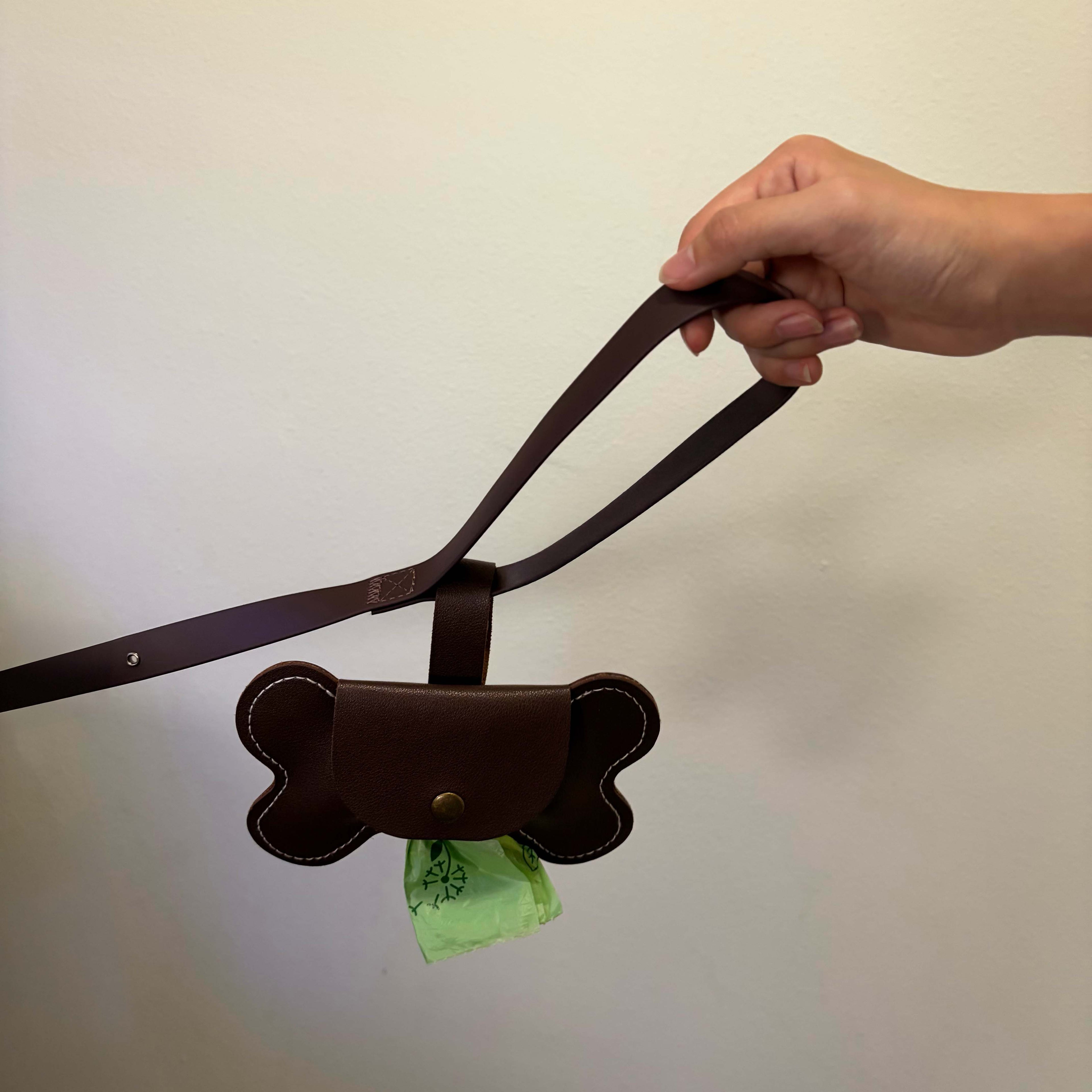 Dog leash with a bone-shaped waste bag holder containing green bags against a plain background
