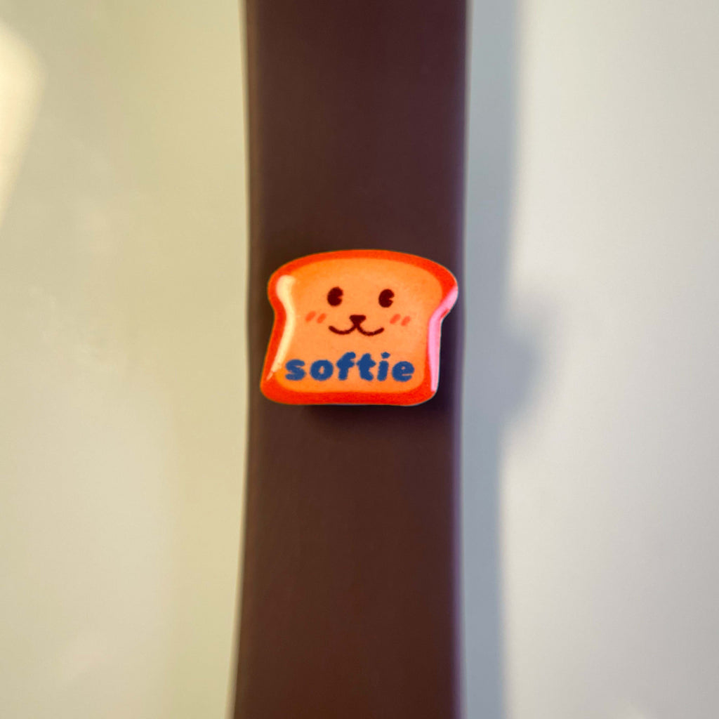 Enamel charm of a smiling toast with 'softie' text on a dog leash or collar.